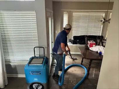 Technician running an extraction hose beside a dehumidifier in a Kernersville living room