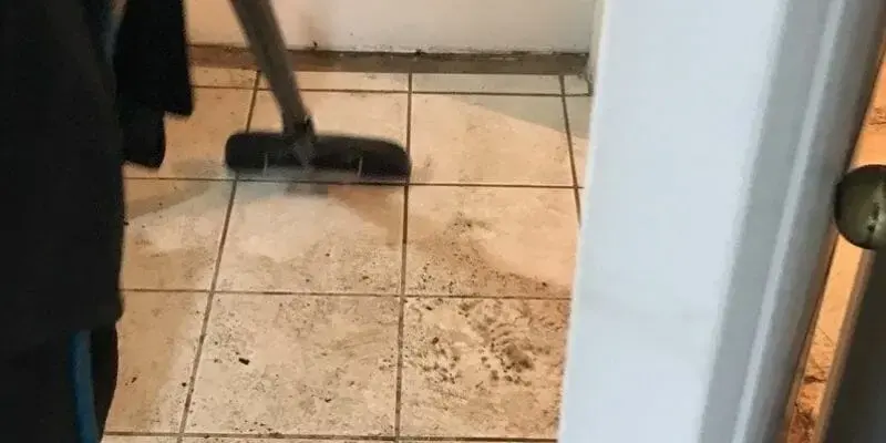 Wet vacuum pulling water off a tile floor beside a leaking appliance in a Kernersville home