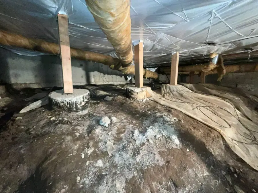 Kernersville crawl space with wet soil, a torn vapor barrier and pier supports under the floor