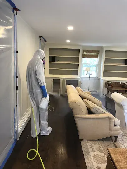 Technician in a full protective suit treating a Kernersville living room during sewage backup cleanup
