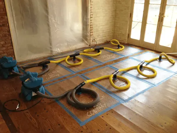 Floor drying mats, hoses and air movers drying a hardwood floor in a Kernersville home